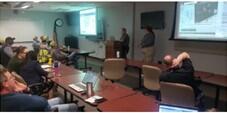 multiple people sitting in a meeting watching a big screen